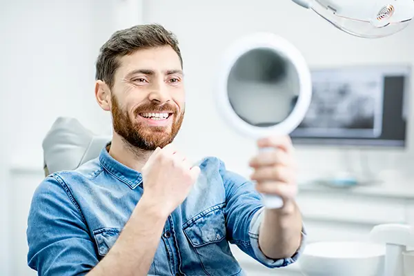 Bearded patient checking out his handsome smile in a mirror while sitting in a dental chair at Century Dental in Hillsboro, OR